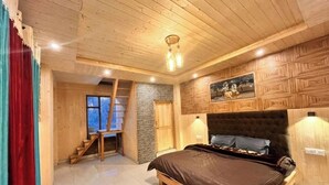 A bedroom with a wooden ceiling, a bed with a brown bedspread, a stone wall, and a wooden staircase. - Apple velley homestay shanghar  (Sainj)