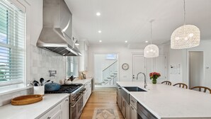 A modern kitchen with white cabinetry, a large island, stainless steel appliances, and a patterned rug. - 619 Carolina / Sleeps 12 / C Escape / Brand New Custom Home With Pool (Isle of Palms)