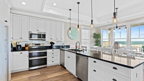 Een moderne keuken met witte kastjes, roestvrijstalen apparatuur en een groot eiland met een zwart aanrecht.