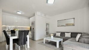A modern living room with a grey sofa, a dining table with chairs, a coffee table, and a kitchen in the background. - Apartment Dijana with private pool (Donji Prolozac)