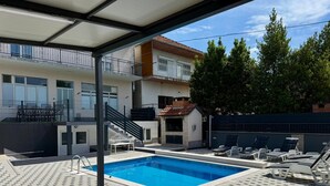 A swimming pool with lounge chairs, a covered area, and a building with a balcony. - Apartment Dijana with private pool (Donji Prolozac)
