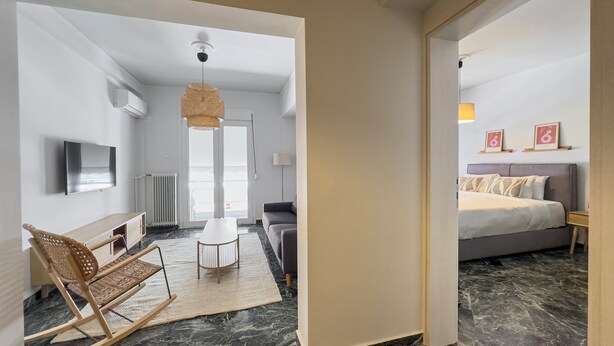 A modern hotel room with a bed, a sofa, a TV, and a dining area with a table and chairs. - Phaedrus Living Koukaki Verdant Marble (Athens)