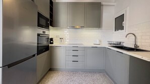 A modern kitchen with stainless steel appliances, white cabinetry, and a tiled backsplash. - Phaedrus Living Koukaki Verdant Marble (Athens)