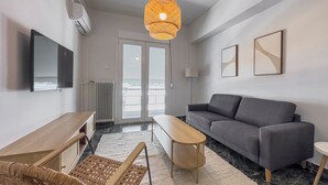 A modern living room with a grey sofa, a wooden coffee table, a wicker chair, a TV mounted on the wall, and a unique hanging light fixture. - Phaedrus Living Koukaki Verdant Marble (Athens)