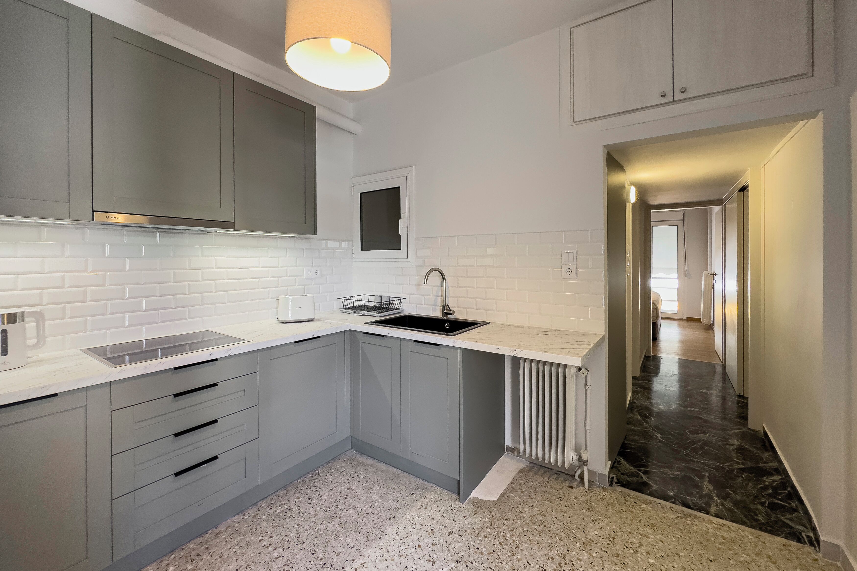Una cocina moderna con armarios grises, una encimera blanca, un lavamanos integrado y una ventana sobre el lavamanos.