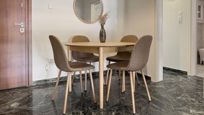 A dining area with a round table, four chairs, a vase with dried plants, and a round mirror on the wall. - Phaedrus Living Koukaki Verdant Marble (Athens)