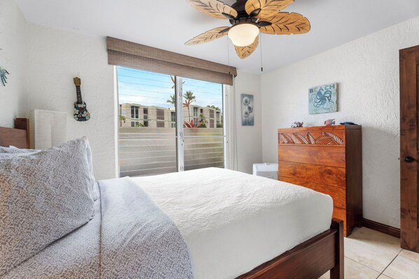 Un dormitorio con cama, cómoda de madera, ventilador de techo y ventana con persianas.