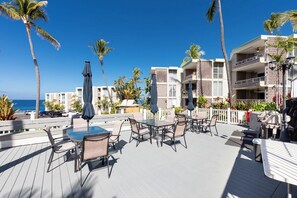 Terraza con mobiliario exterior, palmeras y vista al océano.