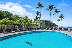 Una piscina con sillones de descanso y palmeras, rodeada de edificios.