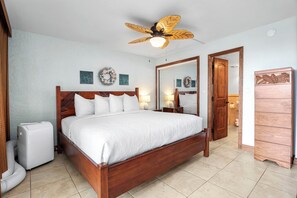 Un dormitorio con cama de madera, ventilador de techo, un calentador pequeño y un aparador.