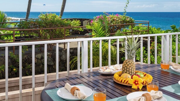 Eine Holzterrasse mit gedecktem Tisch, mit Blick auf einen Strand und das dahinterliegende Meer.