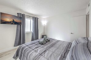 Een slaapkamer met een bed, grijze gordijnen, een bergschilderij en een bedlamp.