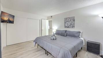 Um quarto com cama, mesa de cabeceira e televisão presa na parede.