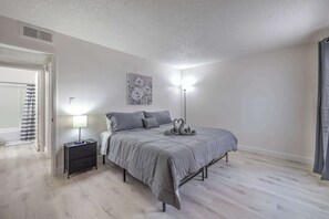 Un dormitorio con cama, mesita de noche, lámpara y un cuadro en la pared.