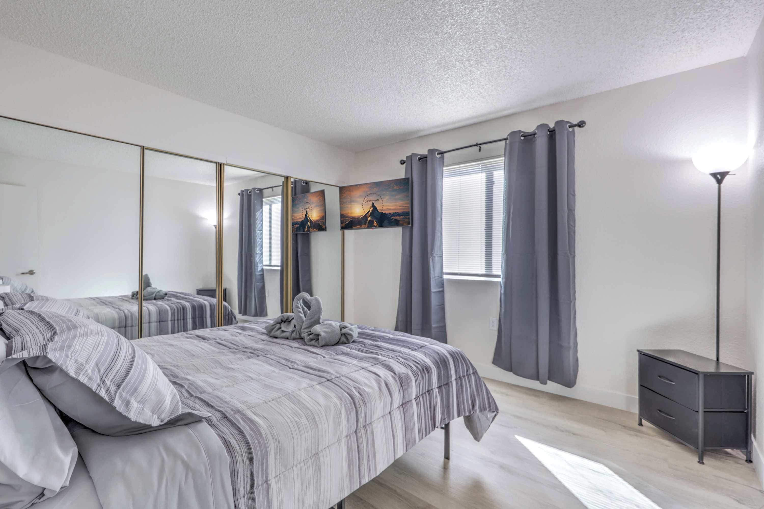 A bedroom with a large bed, a bedside table, a mirror, and a window with curtains.