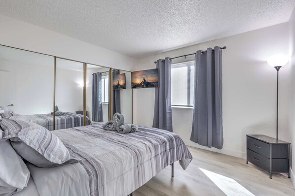 Un dormitorio con una cama grande, una mesita de noche, un espejo y una ventana con cortinas.
