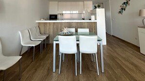 A modern kitchen with white cabinets, a central island, and a dining area with a glass table and white chairs.