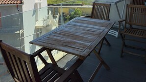A balcony with a wooden table and chairs, overlooking a coastal landscape.