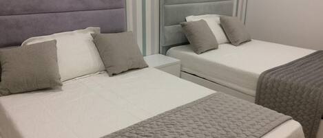 Dos camas con ropa de cama gris y cabeceras, una pared a rayas en el fondo y suelo de madera.