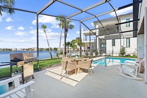 An outdoor patio with a grill, wicker furniture, and a pool.