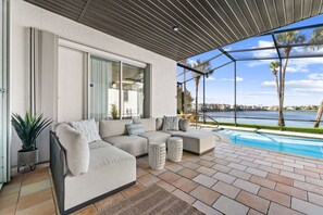 A modern outdoor seating area with a pool, a view of the water, and a clear sky.