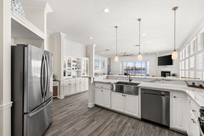 A modern kitchen with a stainless steel refrigerator, white cabinetry, a large island with a sink, and pendant lighting.