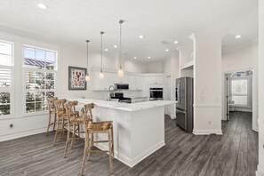 A modern kitchen with white cabinetry, a central island, bar stools, and a large refrigerator.