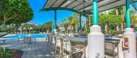 A poolside area with lounge chairs, a bar, and a covered seating area.