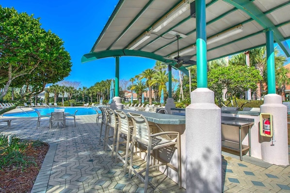 Un espace aménagé au bord de la piscine, avec des chaises longues, un bar et un coin salon abrité.