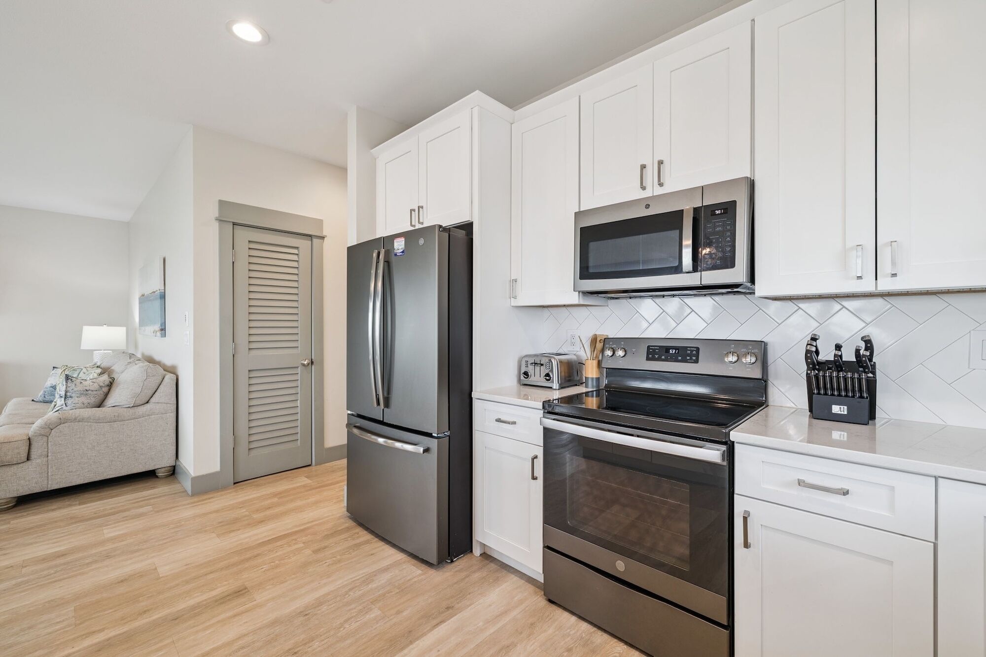 A modern kitchen with white cabinets, a stainless steel refrigerator, a microwave, an oven, and a toaster.