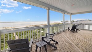 Een overdekt terras buiten met uitzicht op het strand, met twee lounge fauteuils en een tafel.