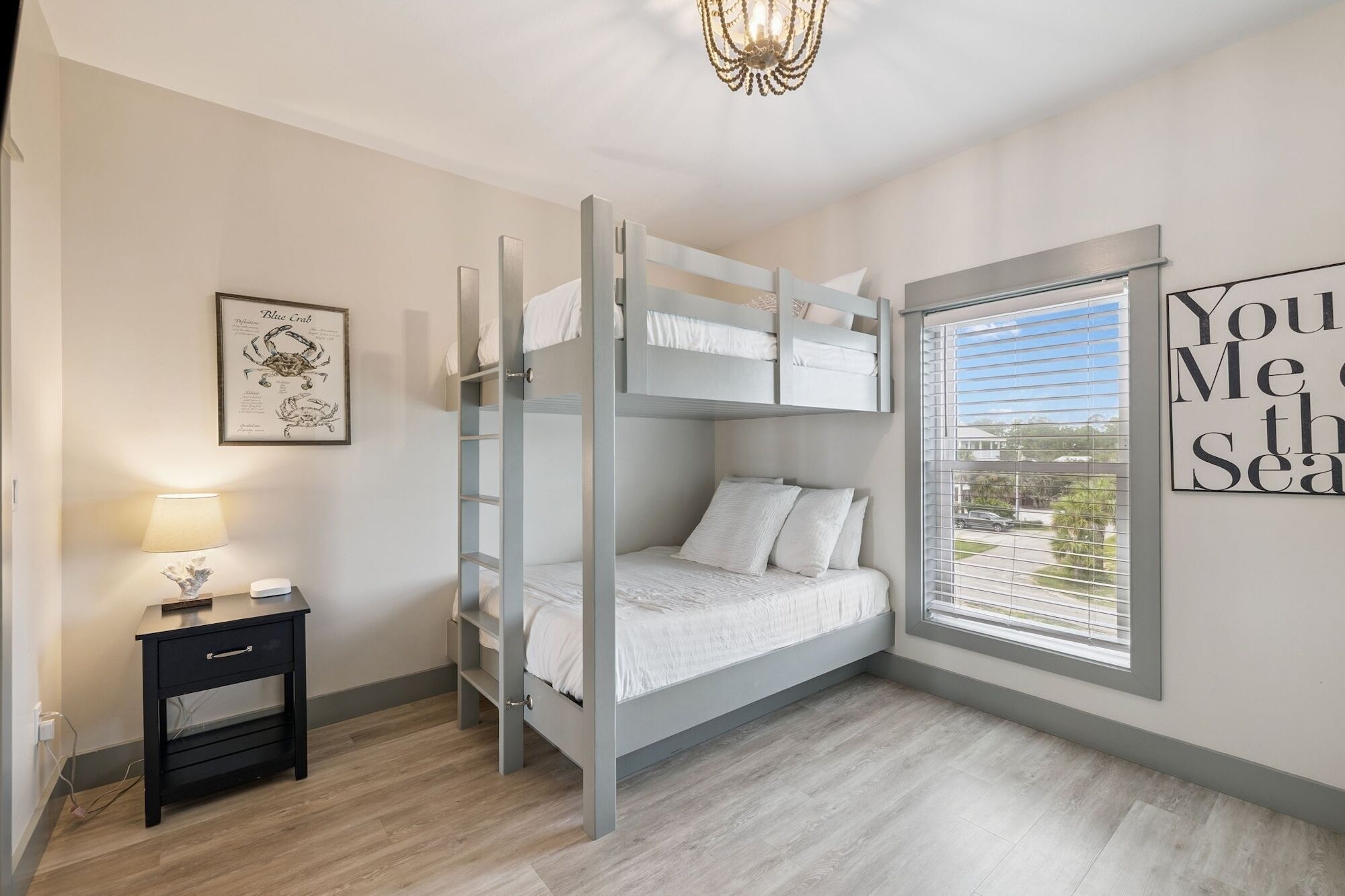 A bunk bed room with a window, a bedside table, and a wall art piece.