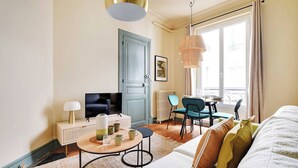 A modern living room with a sofa, coffee table, TV, and dining area. - Cozy Flat 1 BDR / 2P - Marais District (Paris)