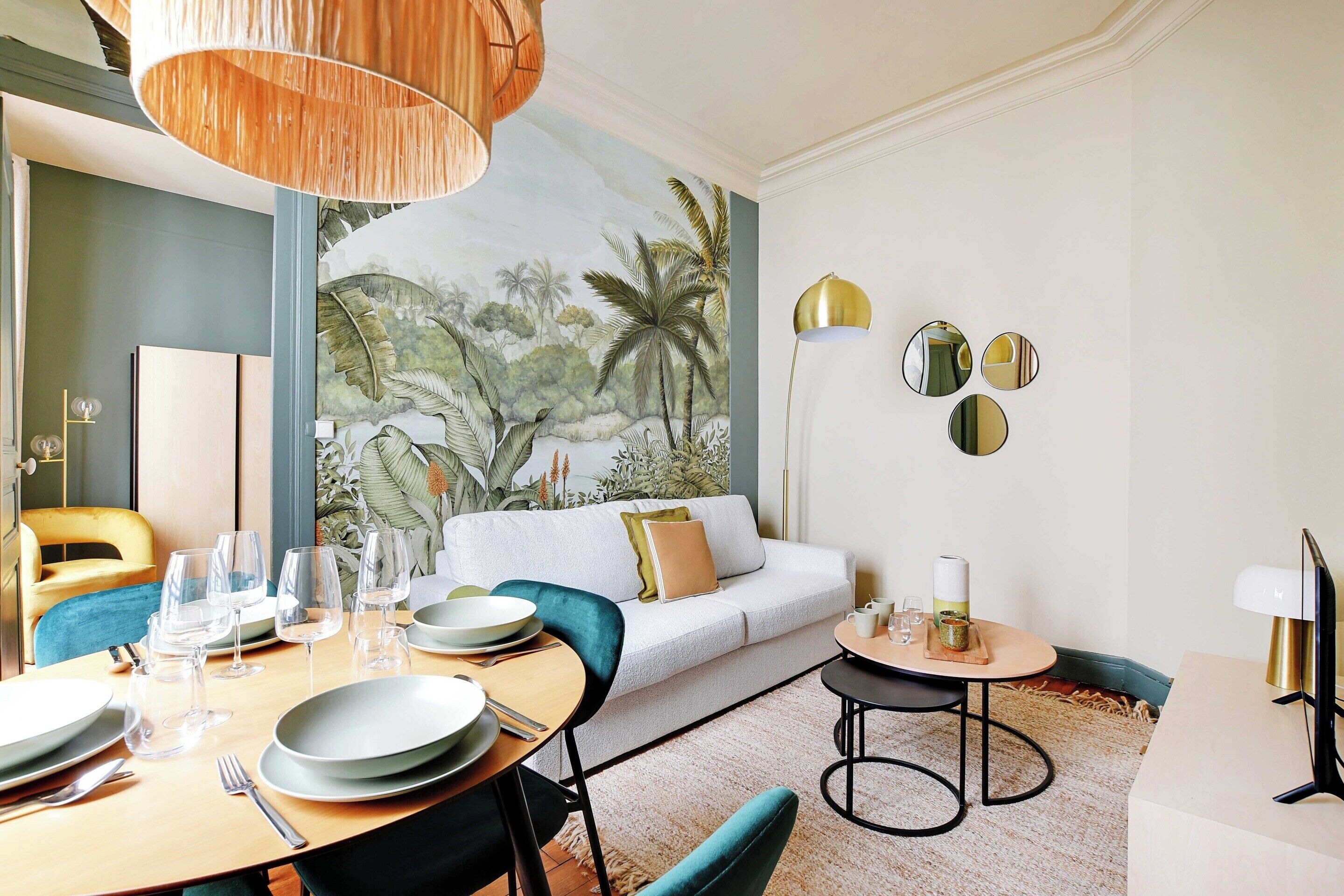 A dining area with a table set for four, a sofa, and a mural of a tropical scene on the wall.