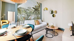 A dining area with a table set for four, a sofa, and a mural of a tropical scene on the wall. - Cozy Flat 1 BDR / 2P - Marais District (Paris)