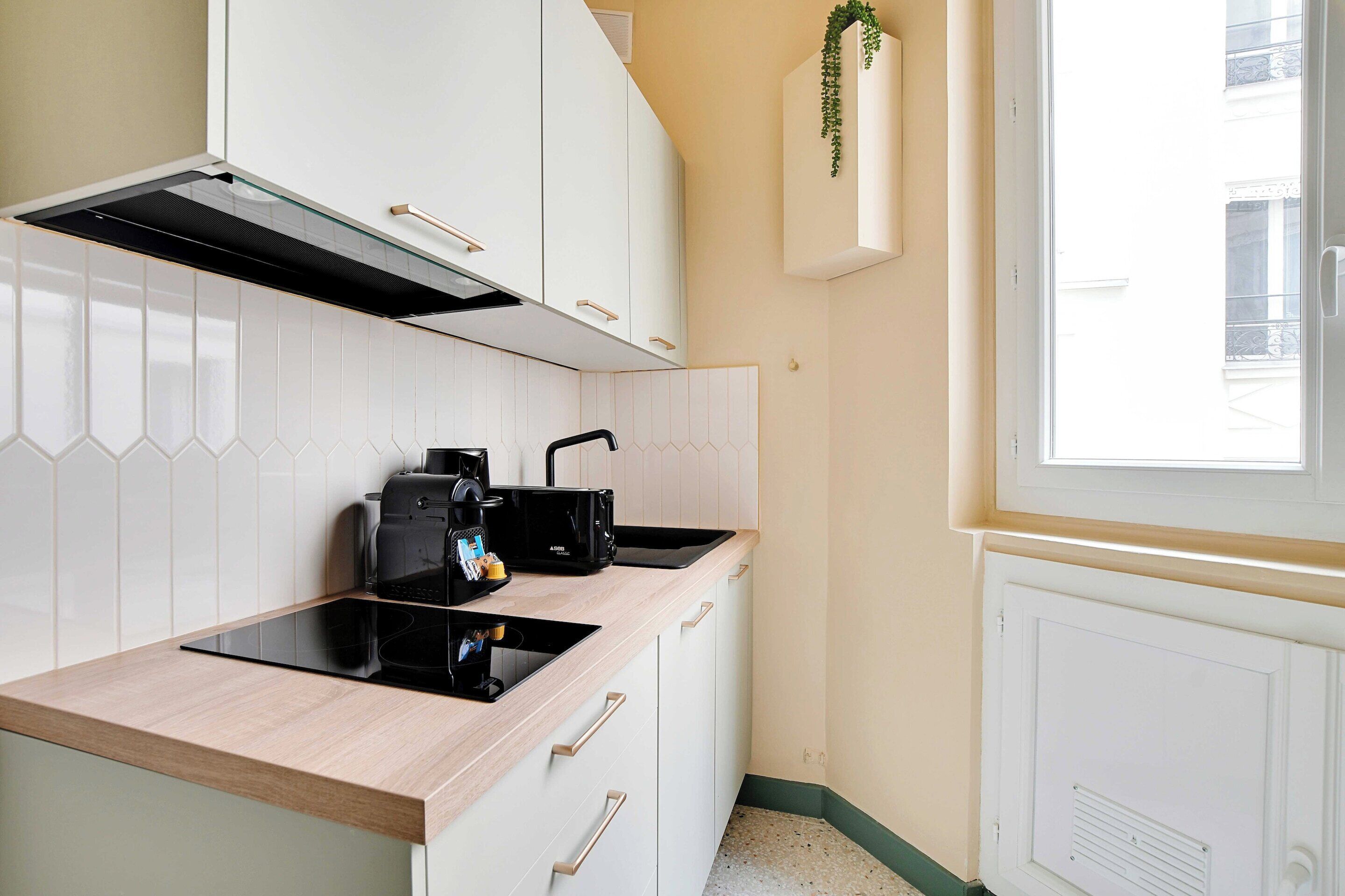 A modern kitchen with a black stove, a coffee maker, and a window with a view of buildings.