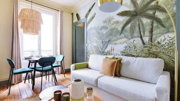 A room with a white sofa, teal chairs, a dining table, and a mural of a tropical scene. - Cozy Flat 1 BDR / 2P - Marais District (Paris)