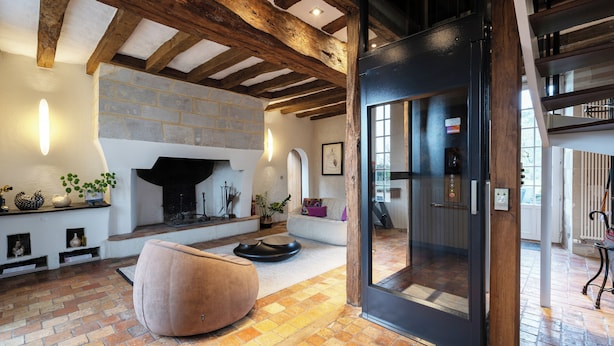 Een ruime woonkamer met zichtbare houten balken, een stenen open haard en een moderne glazen deur die leidt naar een balkon.