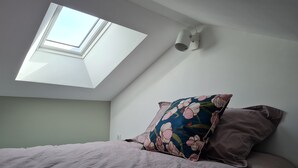 A bedroom with a skylight, a bed with two pillows, and a light fixture on the wall. - Art deco-cooning, (Autun)