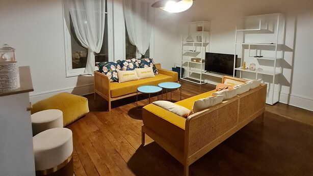 A living room with a sofa, two round tables, and a television. - Art deco-cooning, (Autun)
