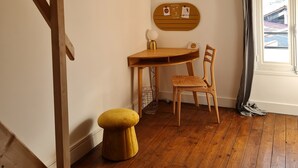 A room with a wooden desk, a chair, a small stool, and a hanging light fixture. - Art deco-cooning, (Autun)