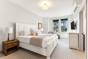A bedroom with a white bed, a bedside lamp, a wicker nightstand, a dresser, and a window with a view of trees. - *NEW* The Hermit: Private Hot Tub, Dog Friendly! (Pacific Beach)