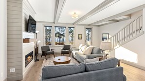 A spacious living room with a fireplace, comfortable seating, large windows, and a staircase. - Seabrook Townhome | Ocean View, Hot Tub | 4BR/8 | Beach 3 Min Walk, Garage (Pacific Beach)