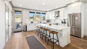 A modern kitchen with white cabinetry, a stainless steel refrigerator, and a central island with bar stools. - Seabrook Townhome | Ocean View, Hot Tub | 4BR/8 | Beach 3 Min Walk, Garage (Pacific Beach)