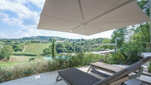 A patio with two lounge chairs and a large umbrella, overlooking a vineyard and a swimming pool. - Belmonte Spereto Pool Nature Montaione  (Montaione)