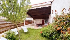 A covered patio area with a table and chairs, surrounded by greenery and a wooden fence. - Old 18th century stable for 4 people (VERGEROUX)