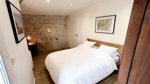 A bedroom with a stone wall, a bed with white bedding, a framed picture on the wall, and a wooden door. - Old 18th century stable for 4 people (VERGEROUX)