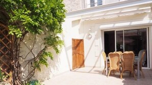 A patio with wicker chairs and a table, a wooden door, and a white wall. - House in the very center - 350 m from the main beach - 6 people. (FOURAS)
