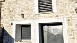Ein Steinhaus mit einer Metalldür, Rollläden, einem kleinen Fenster und einer Wandleuchte.