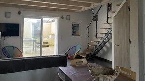 Ein Zimmer mit Esstisch, Stühlen, Fernseher, einer Treppe und einer zur Außenseite führenden Tür.
